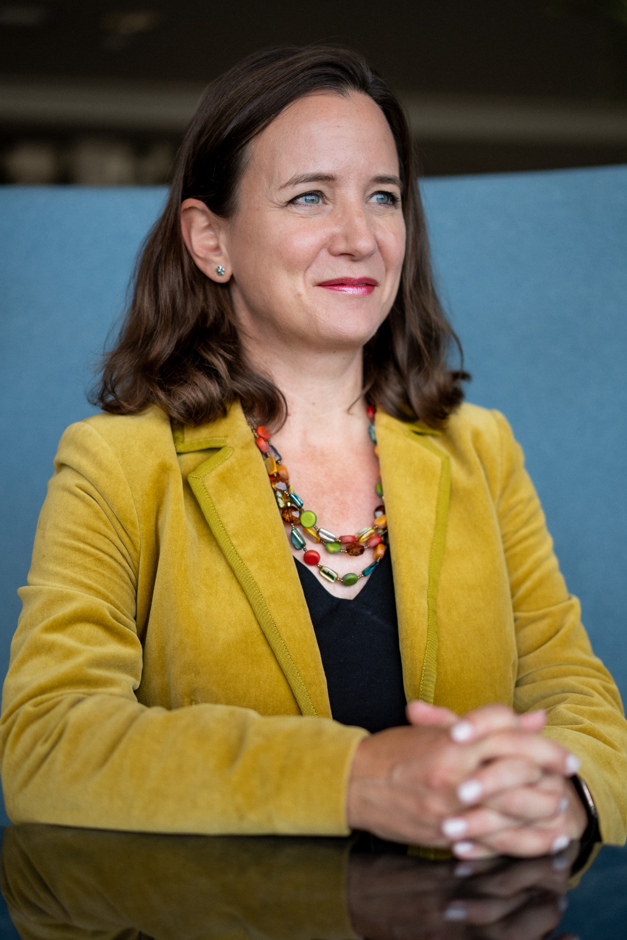 Kathryn Kernick seated at a table in a mustard jacket, smiling